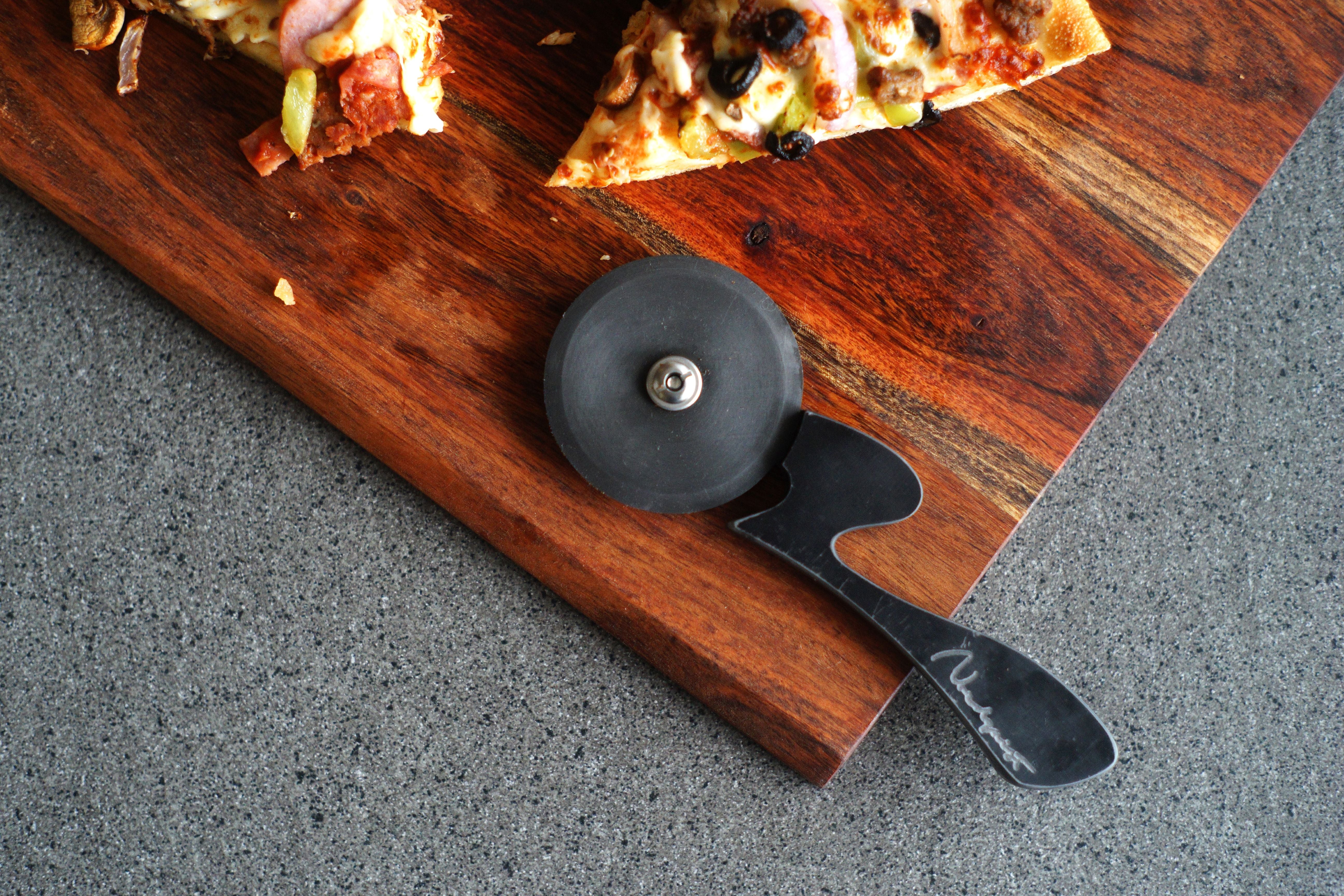 Carbon steel pizza cutter on board with pizza 